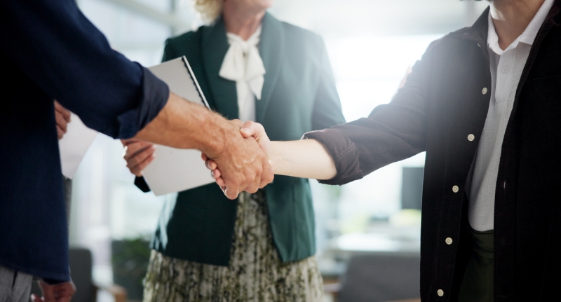 Duas pessoas unindo as mãos em em gesto de parceria, representando a conexão e o alinhamento entre stakeholders de um negócio.