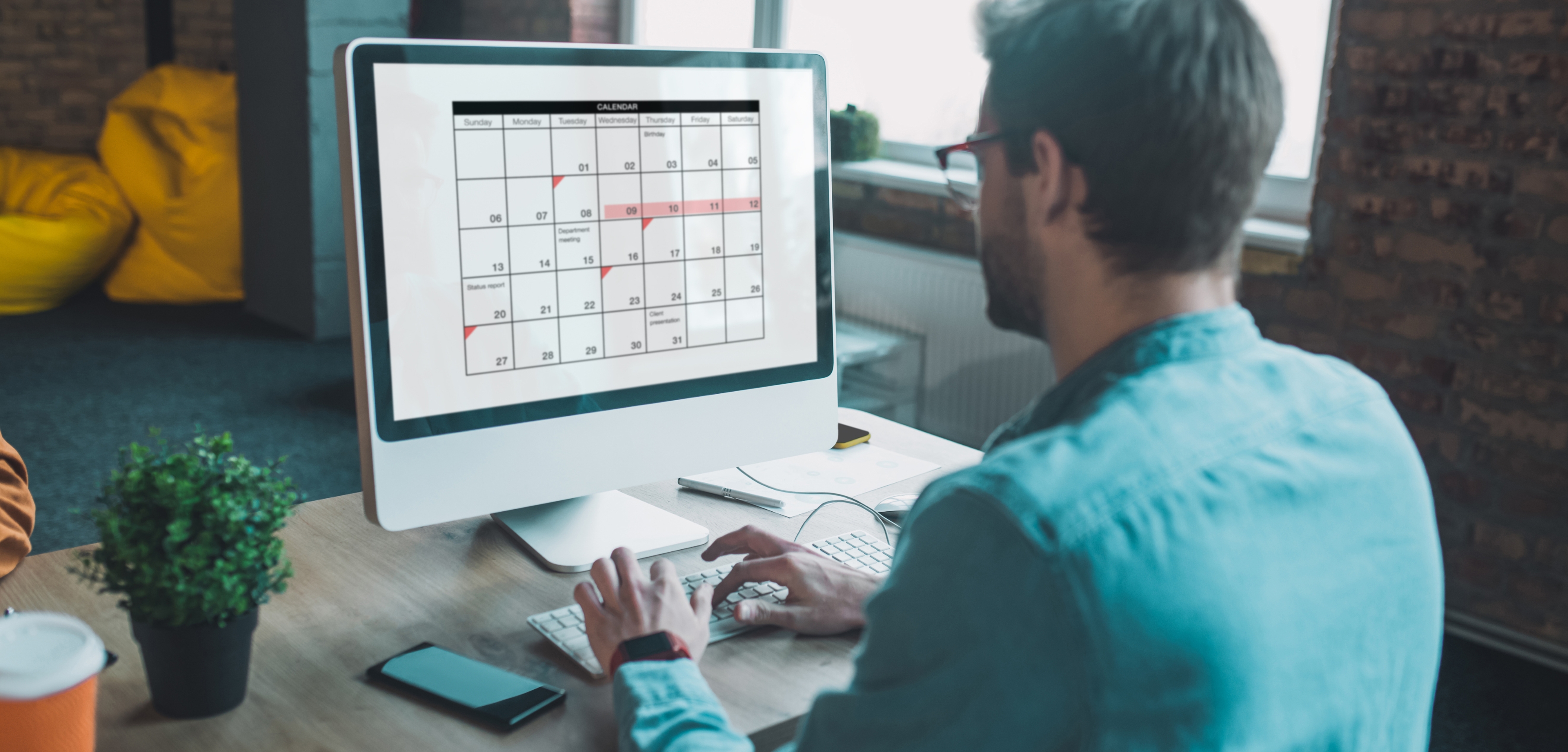 A imagem apresenta um homem sentado em frente a um computador, com um calendário aparecendo na tela.