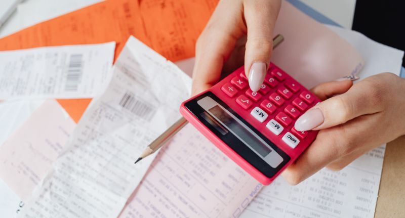 Pessoa fazendo contas em uma calculadora enquanto consulta informações sobre renegociação de dívidas