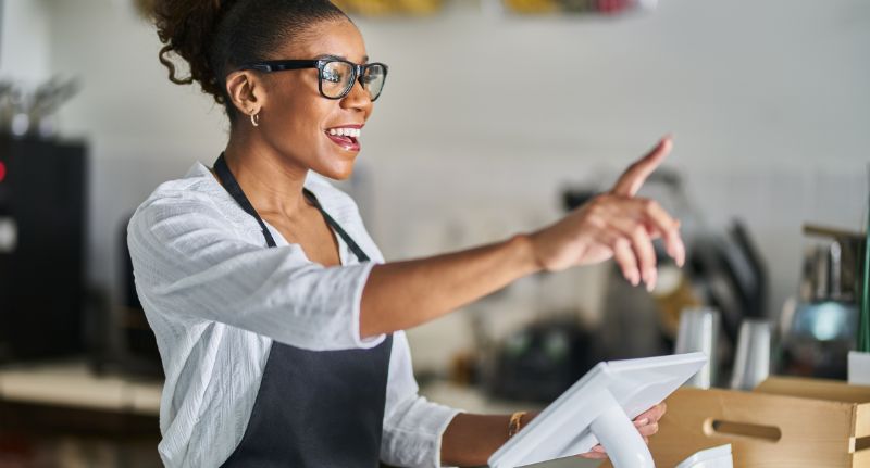 Mulher negra em um caixa de atendimento acenando para clientes.