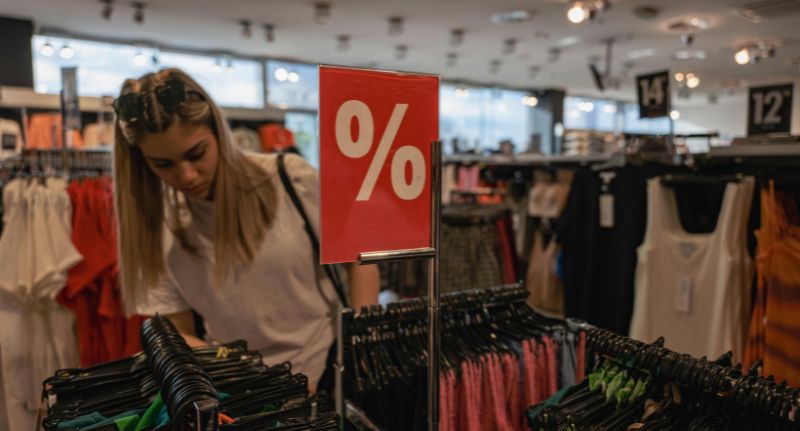 Mulher escolhendo roupas em uma loja de departamento com etiquetas de desconto durante uma promoção.