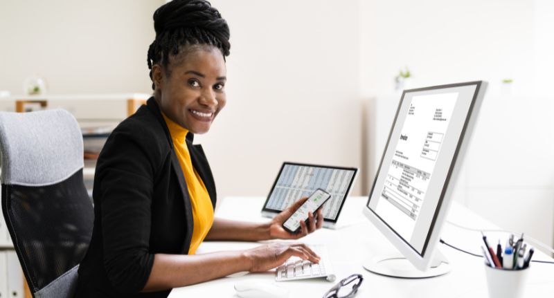 a imagem mostra uma mulher com celular na mão fazendo nota fiscal em frente ao computador