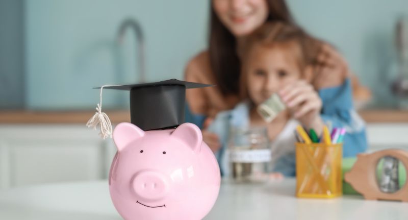 A imagem faz referência ao planejamento financeiro familiar ao mostrar uma mãe e sua filha guardando dinheiro.