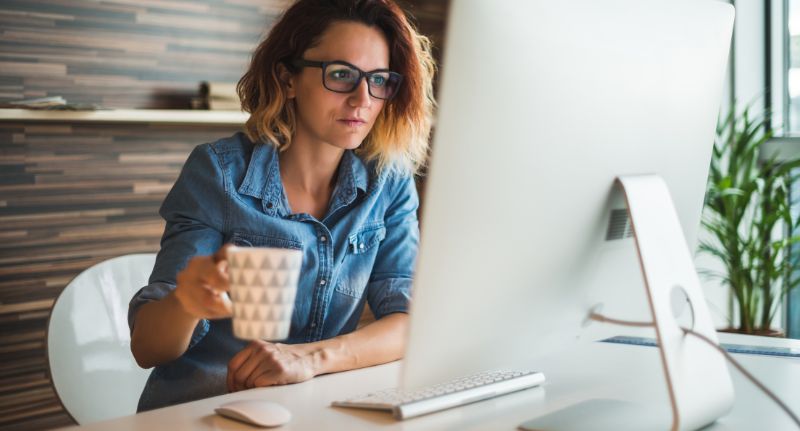 mulher tomando café e verificando sua restituição do imposto de renda no computador