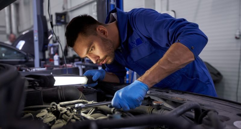 A imagem mostra um homem mexendo em um carro. Ele é um mecânico, portanto, está mexendo no escapamento do carro.