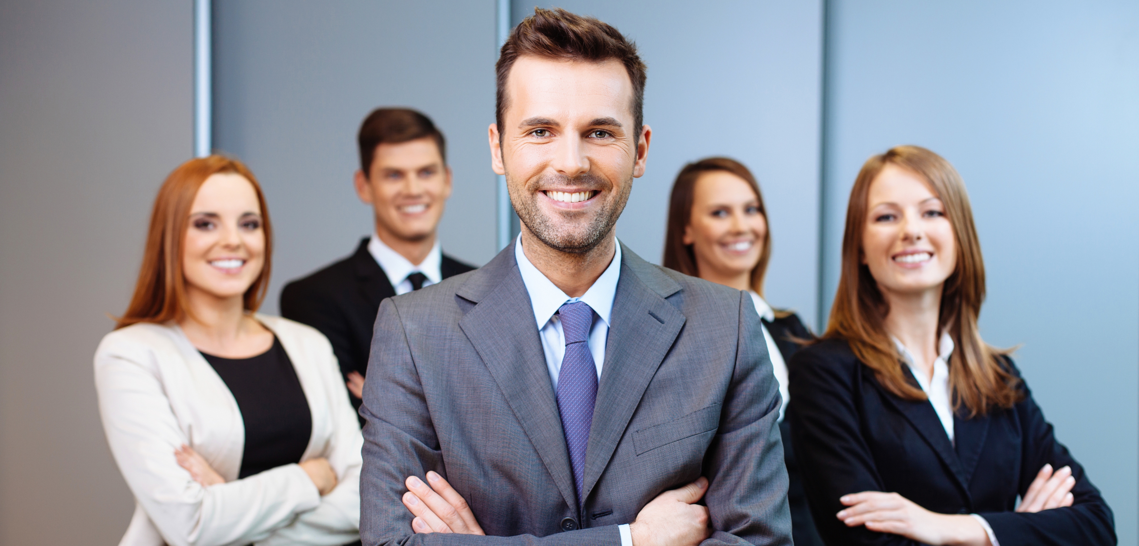 A imagem apresenta 5 pessoas, homens e mulheres, vestidos em trajes sociais. Todos estão sorrindo e estão de braços cruzados, representando pessoas de negócios, como empreendedores.