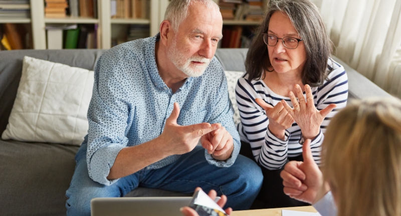 Um casal de idosos faz contas com as mãos diante de uma corretora de previdência privada.